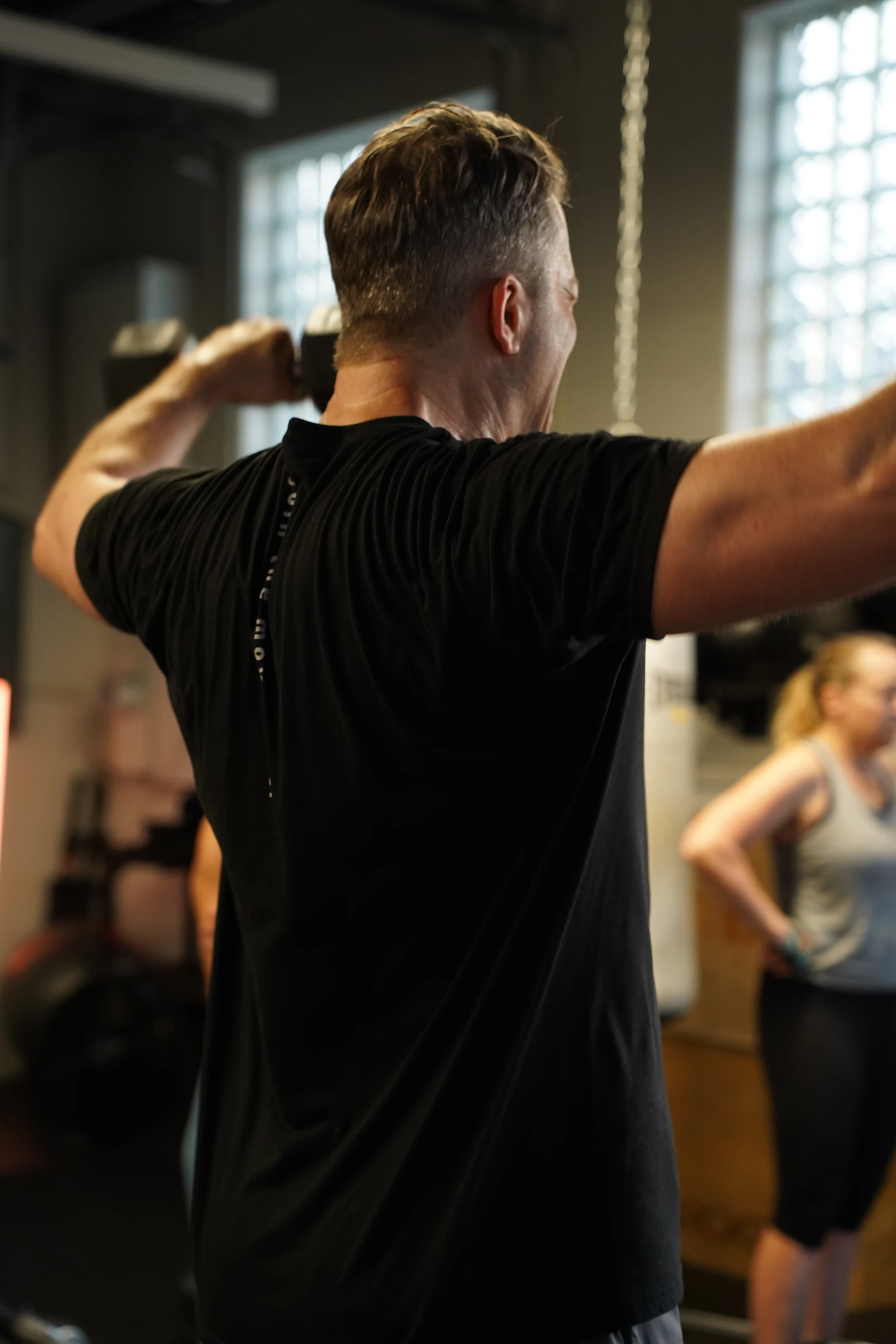 Member pressing dumbbells overhead during strength class at Move Detroit